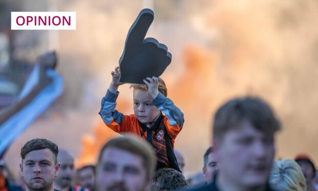 photo shows a small boy on an adult's shoulders surrounded by Dundee United football fans with tangerine coloured smoke in the air.