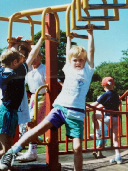 Photo shows the writer Alan Gillespie as a golden haired little boy swinging on a climbing frame in Glenrothes on a sunny day. 