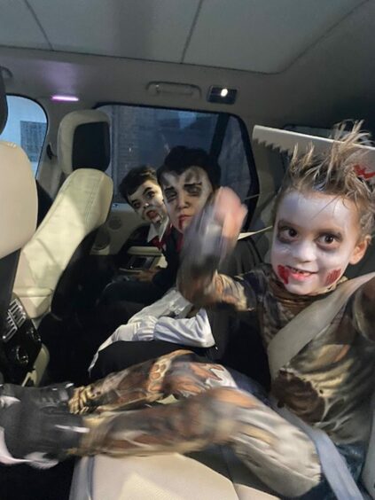 Photo shows three small boys in fancy dress and face-paint in the back seat of a car.