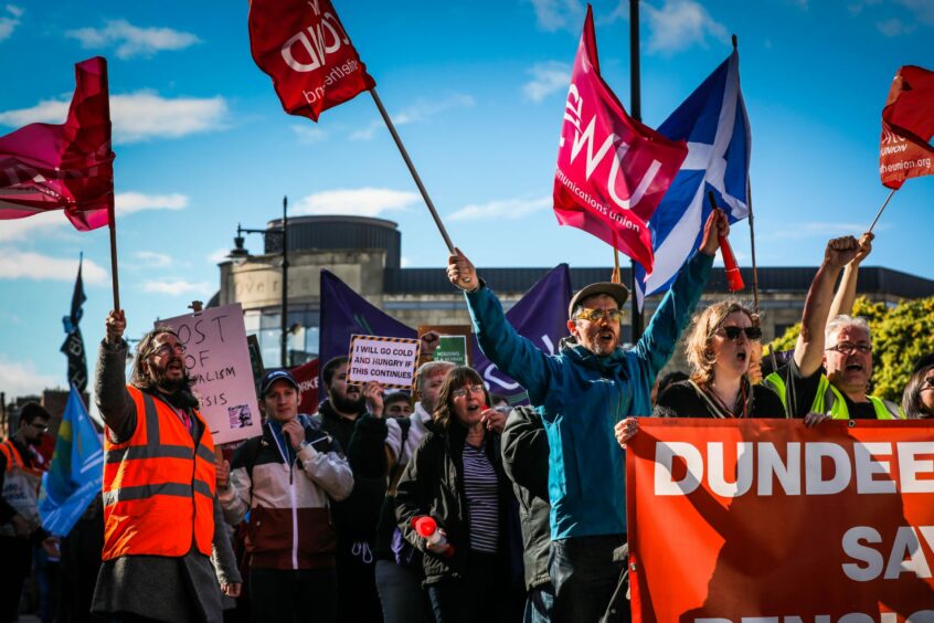 Photo shows a large crowd marching through the centre of Dundee, waving banners and placards with slogans such as 'I will go cold and hungry if this continues'.