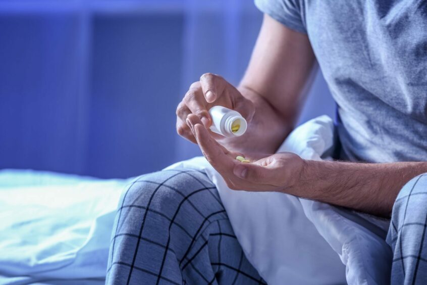 A man sitting on a bed pouring sleeping pills into his hand.