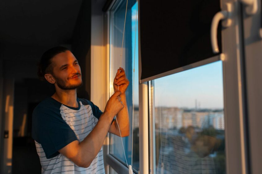 Man closing blinds at sunset.