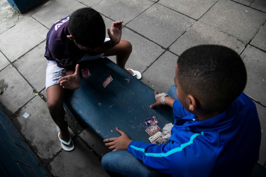 Photo shows two children sitting on a bench with a pile of Panini football stickers between them.