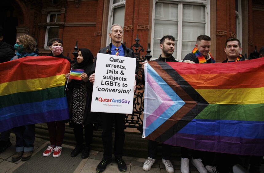 Photo shows LGBT+ activist Peter Tatchell and others with LQBTG and trans flags holding a demonstration outside the Qatar Embassy