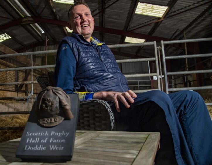 photo shows Doddie Weir in his wheelchair, inside a farm shed, with a sculpted memento to mark his induction into the Scottish Rugby Hall of Fame in 2020.