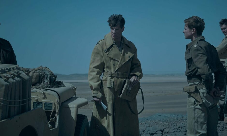 Connor Swindells as David Stirling in the action drama SAS Rogue Heroes. He is standing beside a Jeep in the desert while two men look on