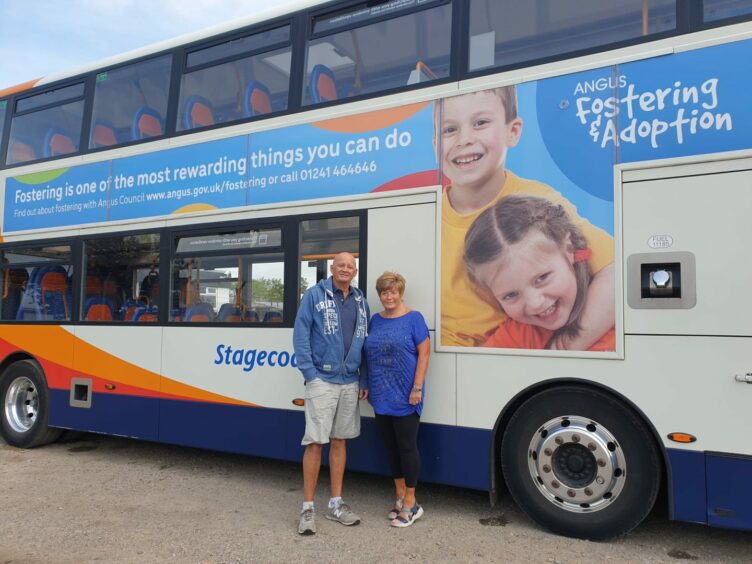 A couple of foster carers pose in front of a bus that advertises fostering and adoption in Angus