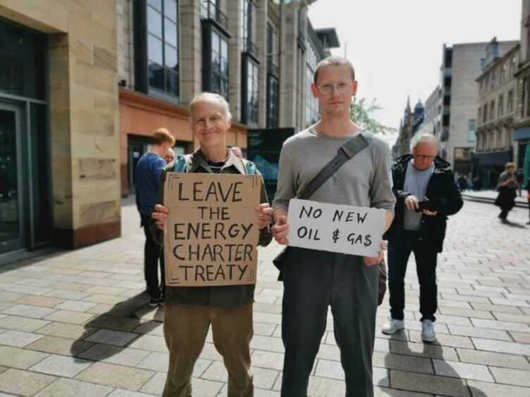 The Tayside climate activist, Adrian Johnson, alongside his son, Dan Johnson, at a recent protest. They are standing on the street holding signs that read "Leave the energy charter treaty" and "no new oil & gas". 