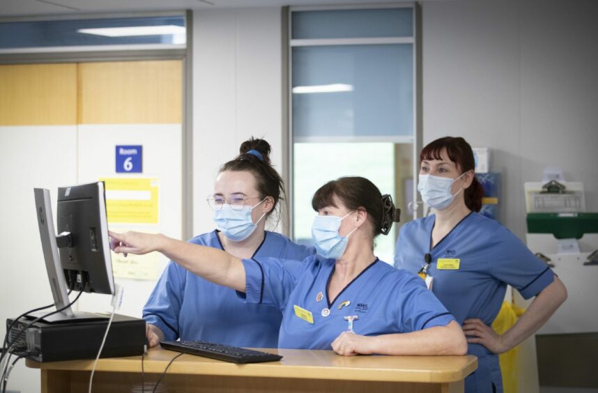 photo shows three nurses looking at a computer on a ward.