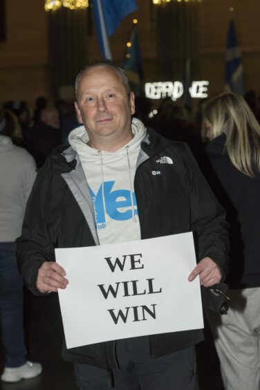 Man in Yes hoodie holding a piece of paper with the word 'We will win' in capital letters.