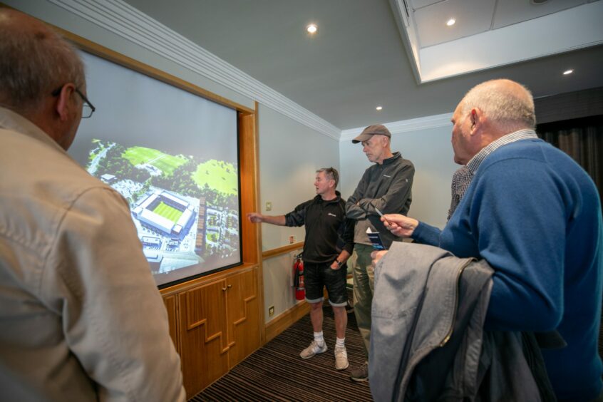 photo shows men looking at a large screen showing images of Dundee FC's proposed new stadium at Camperdown.