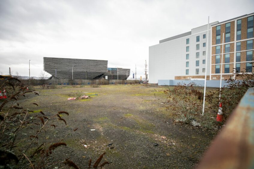 Photo shows weeds growing out of a wide open piece of land next to the V&A Dundee and Agnes Husband House at Dundee Waterfront.