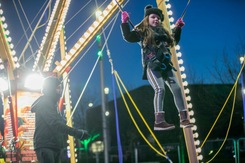 Photo shows a little girl in a harness bouncing on a trampoline surrounded by bright lights in Dundee's Slessor Gardens.