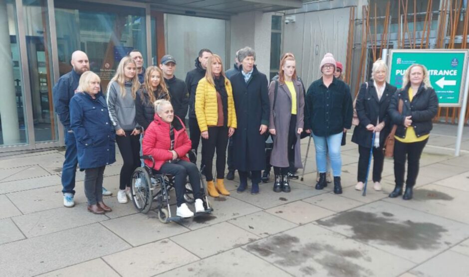 photo shows a group of former patients of Sam Eljamel, some with walking sticks, one in a wheelchair, outside the Scottish Parliament in Edinburgh.