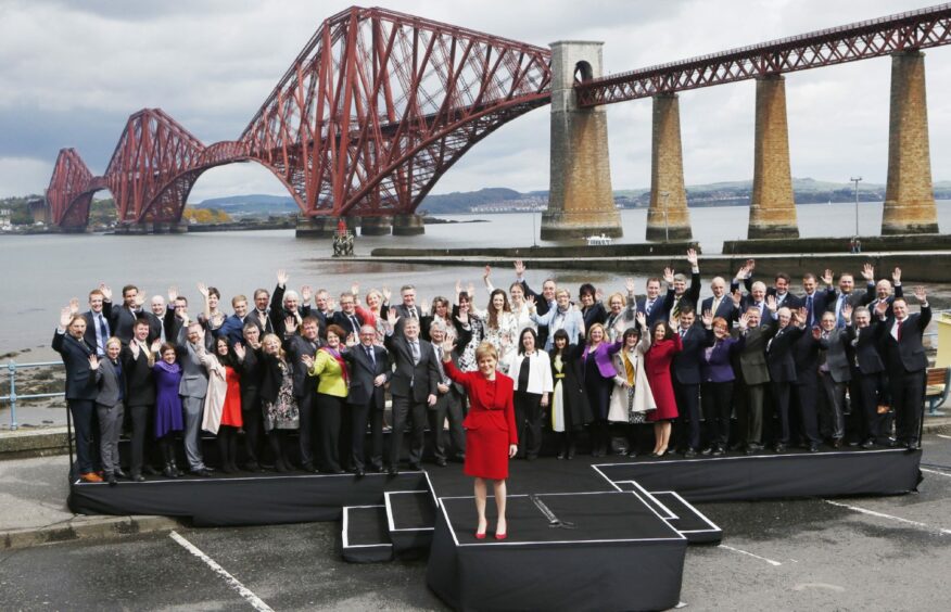 Photo shows Nicola Sturgeon and a large gathering of MSPs waving to the camera in front of the Forth Bridge.