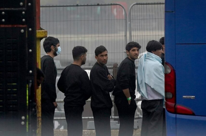 photo shows a group of six men thought to be migrants boarding a coach in the Border Force compound in Dover, Kent.