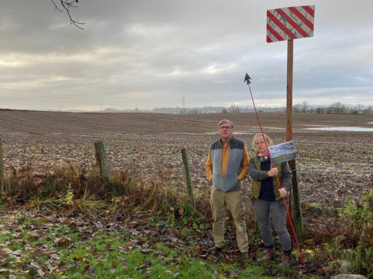 Chris and Roz Button next to their marker in Coupar Angus suggesting the height of the solar panels. 