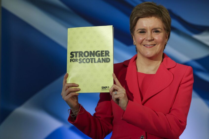 photo shows Nicola Sturgeon holding the SNP manifesto document, titled Stronger for Scotland, in front of a saltire flag.