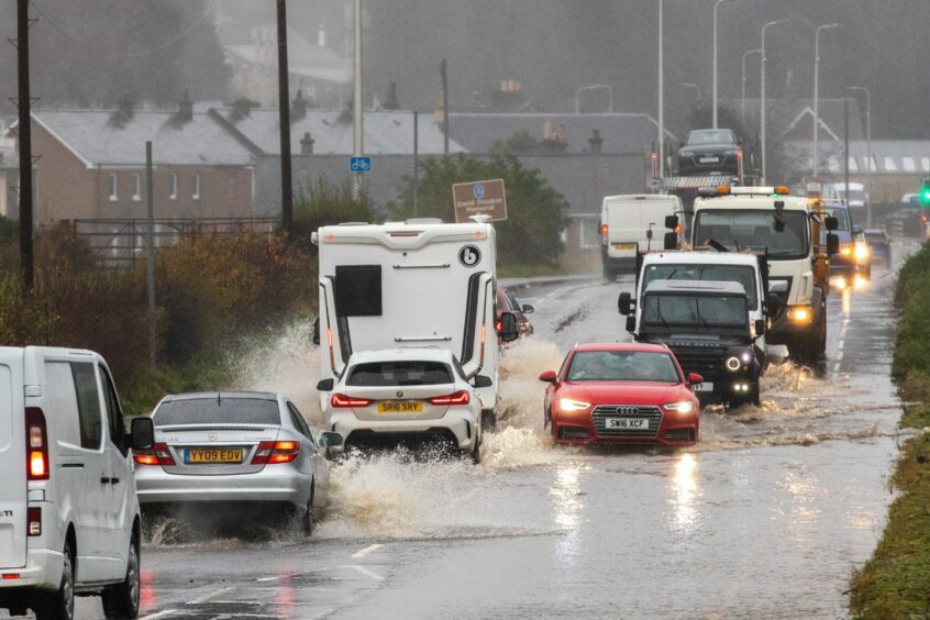 cars and lorries driving through deep flood water near Scone