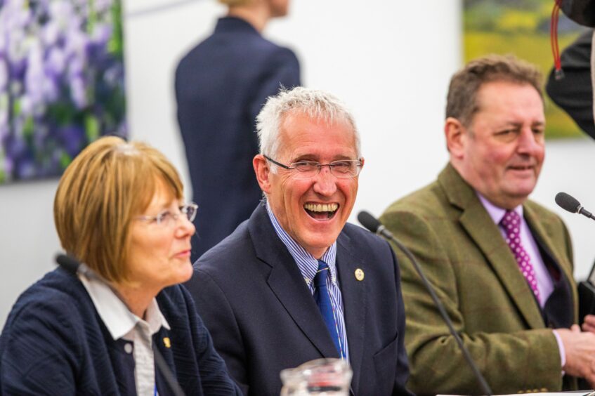 Crawford Reid smiling seated next to two other councillors at a meeting