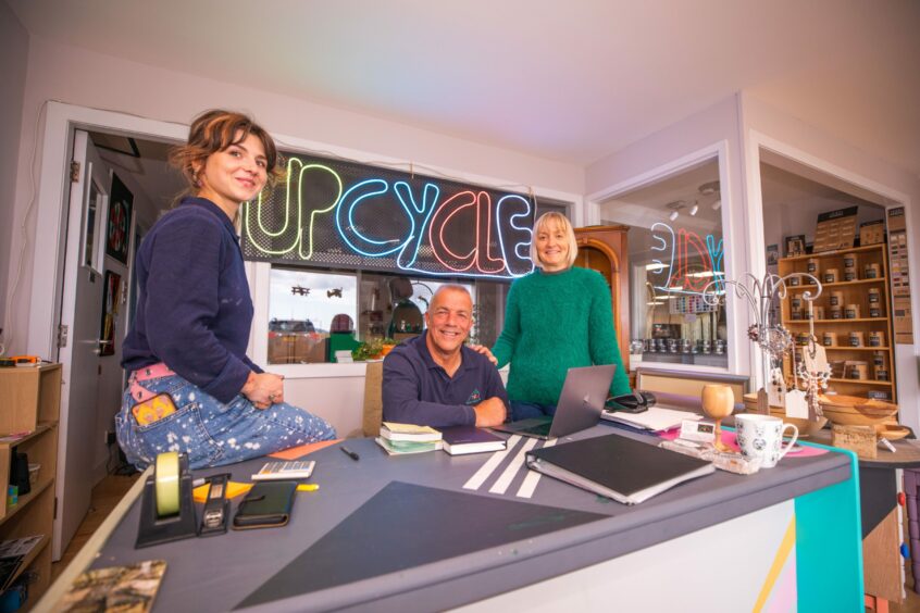 Three upcyclers from the Tayside Upcycling & Craft Centre. Diva sits on the edge of a table, with Alfie and Sarah behind it. The trio have shared their upcycling tips over November. 