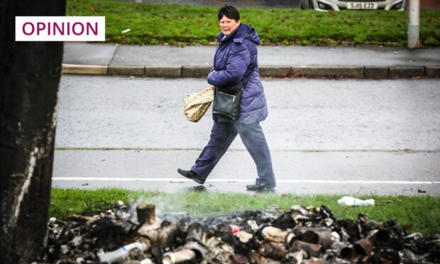 photo shows a woman walking past a pile of charred, smoking debris.