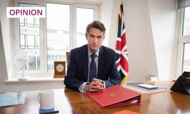 photo shows Gavin Williamson seated behind a desk with a union jack in the background.