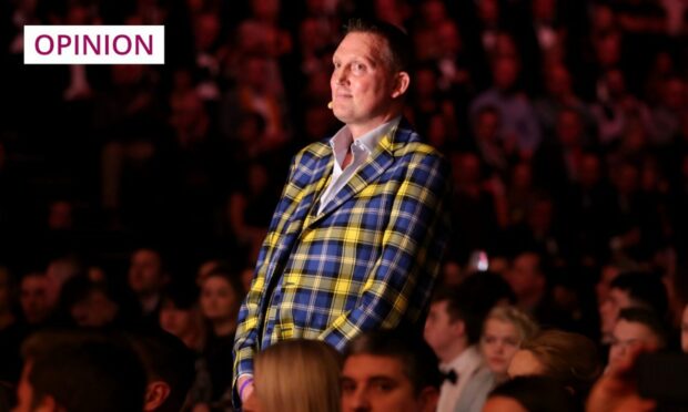photo shows Doddie Weir in trademark tartan suit standing in the spotlight among an audience.