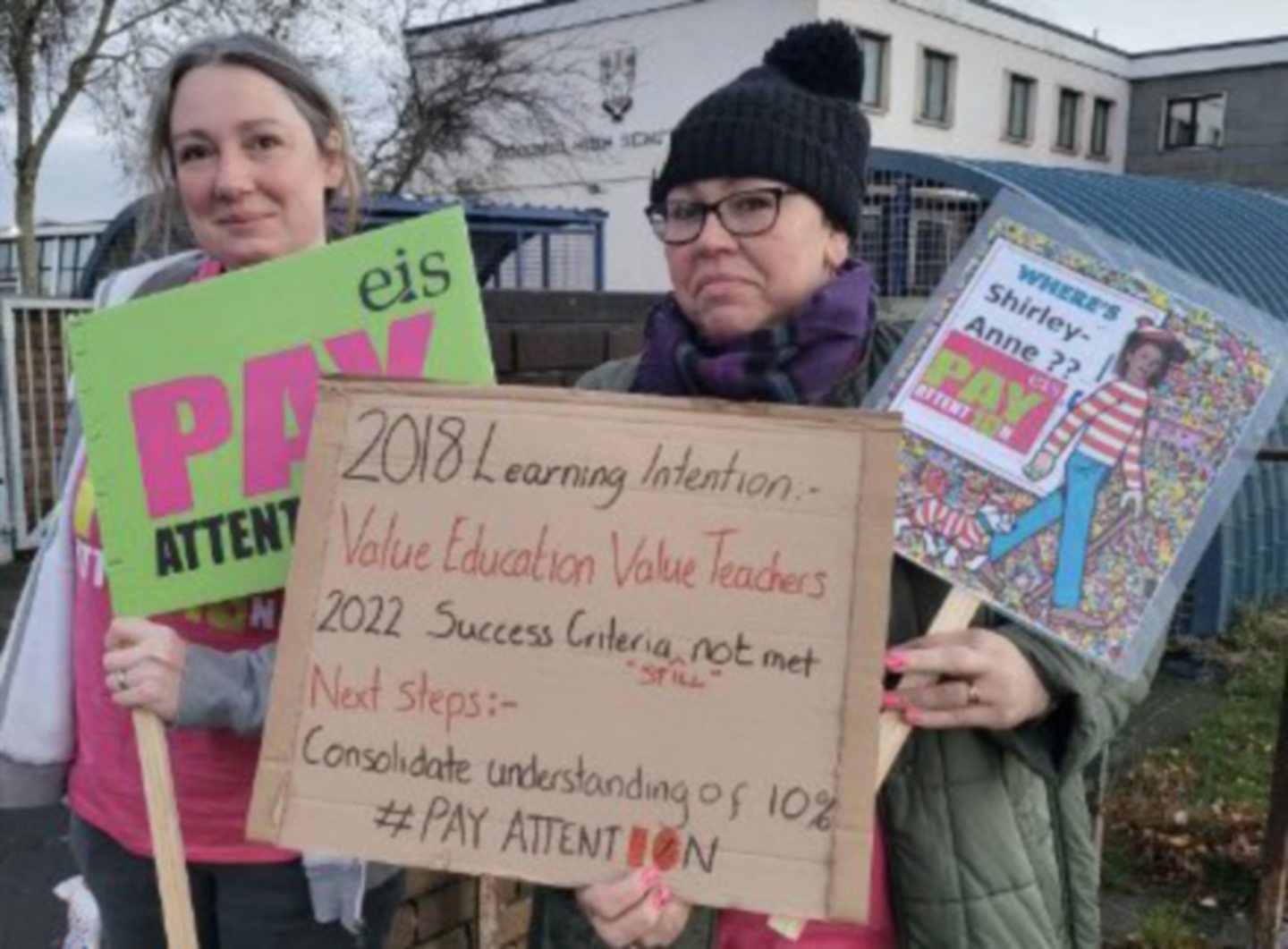 Teachers hold up signs about pay during strike.