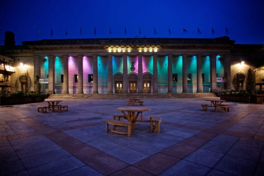 The Caird Hall lit up at night time in pinks and greens.