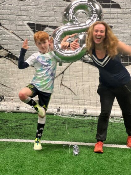 Photo shows Martel Maxwell and son, in football kit, standing in front of a goal with an eight-shaped balloon.
