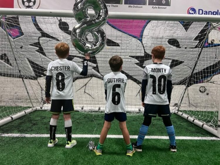 three small boys with their backs to the camera and their names and ages on the back of their football shirts.