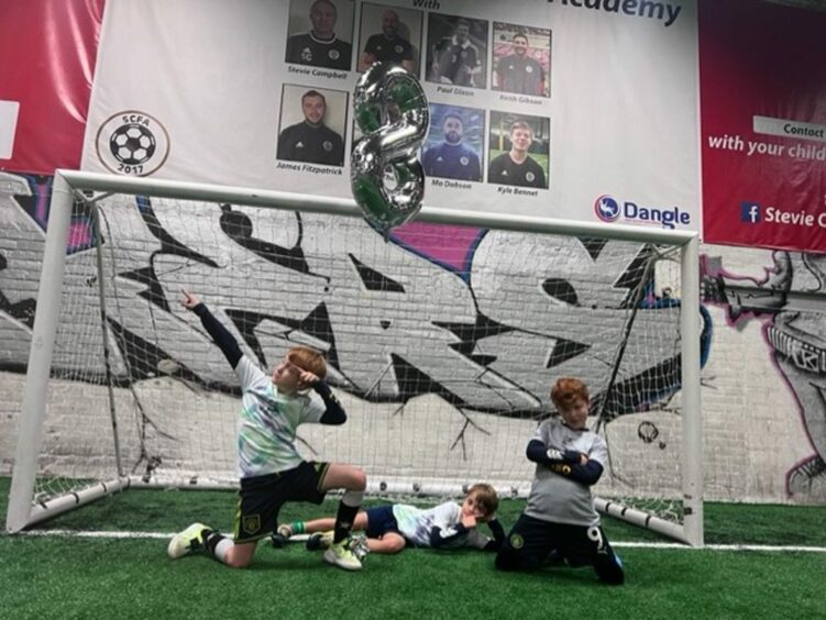 Martel Maxwell's three sons posing in front of a fotball goal.