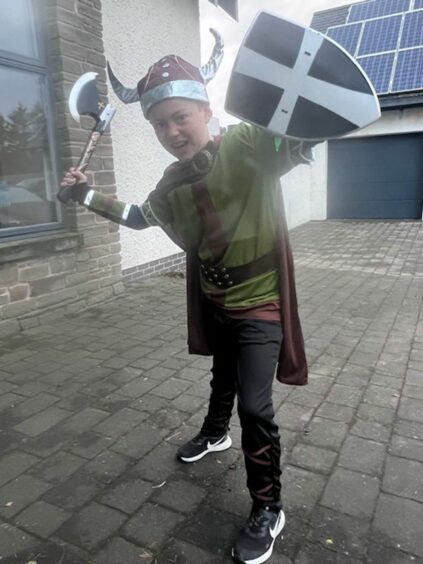 photo shows a small boy wearing a viking helmet and waving a shield and axe.