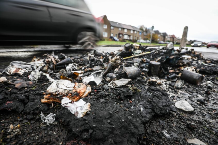 photo shows charred debris lying in the gutter as a car drives past.