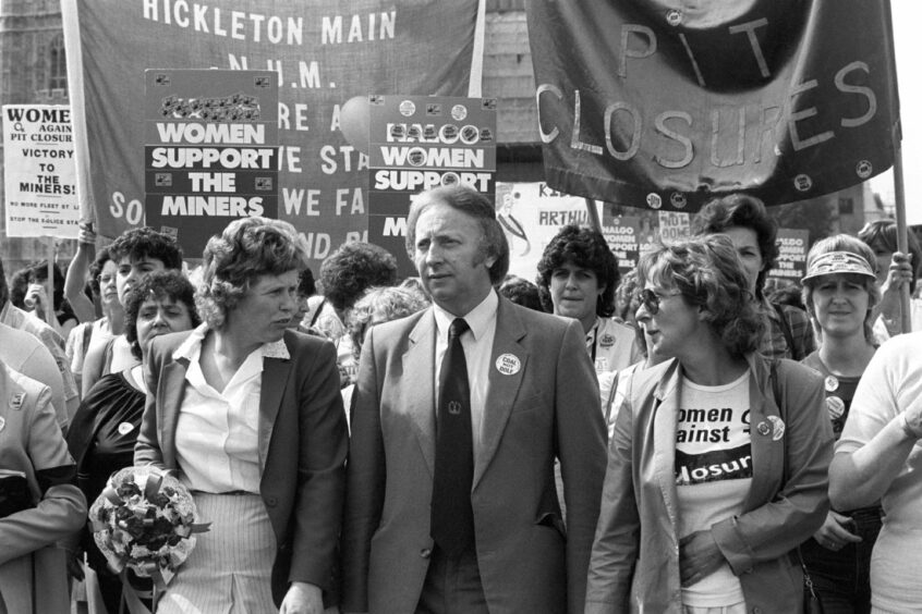 black and white photo shows Arthur Scargill smarching with striking miners' wives.