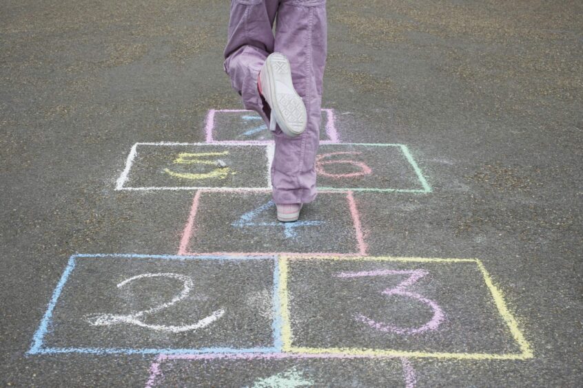 photo shows a child from behind skipping on a hopscotch grid.