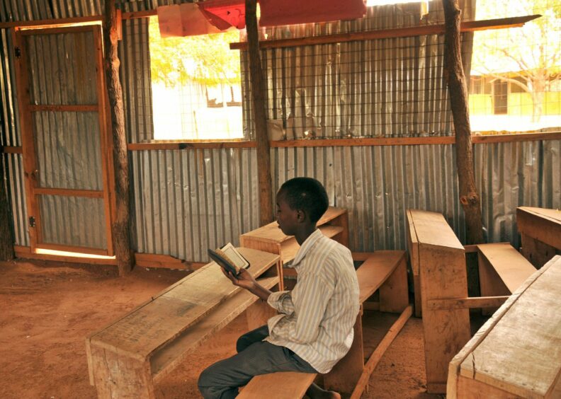 photo shows a young boy reading a book at a wooden bench in a corrugated iron classroom in Somalia.