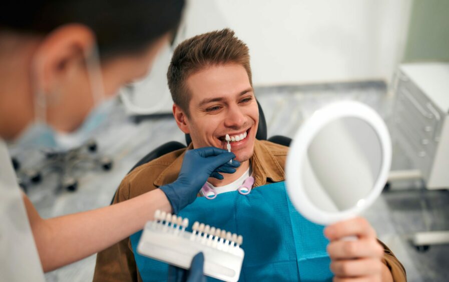  closeup of a dentist with tooth color samples choosing a shade for a male patient's teeth in a dental clinic 