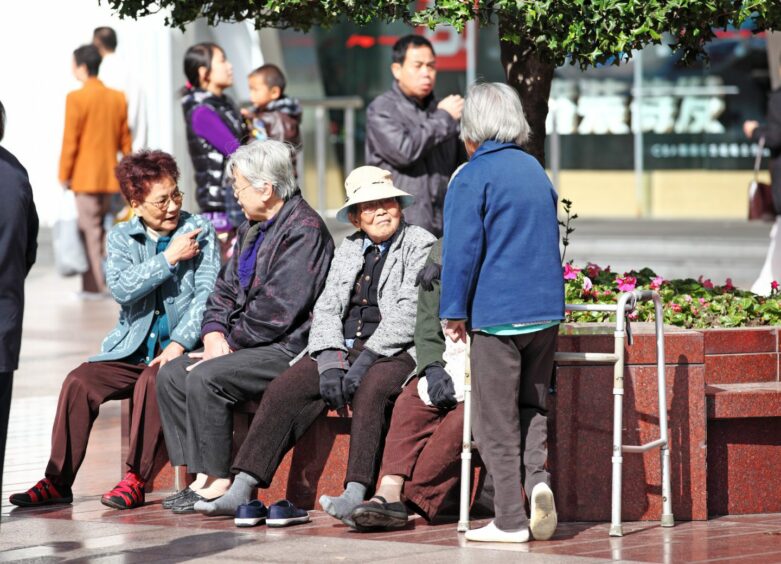 photo shows a group of older Chinese women sitting on benches chatting.