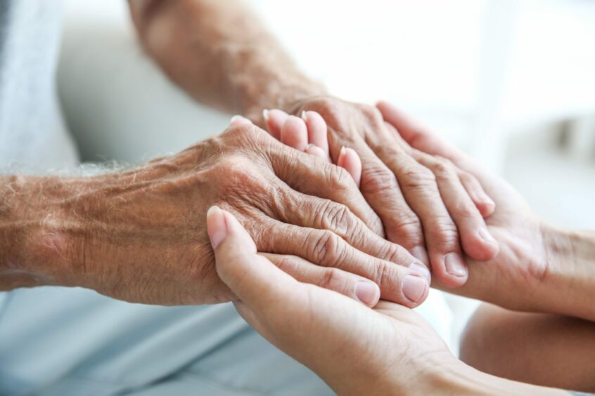 photo shows a young woman's hands holding the hands of an elderly man.