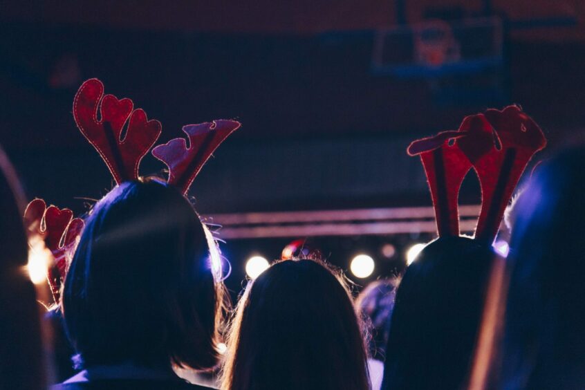 Photo shows the heads of little girls wearing antlers, under stage lights and looking out into an audience.
