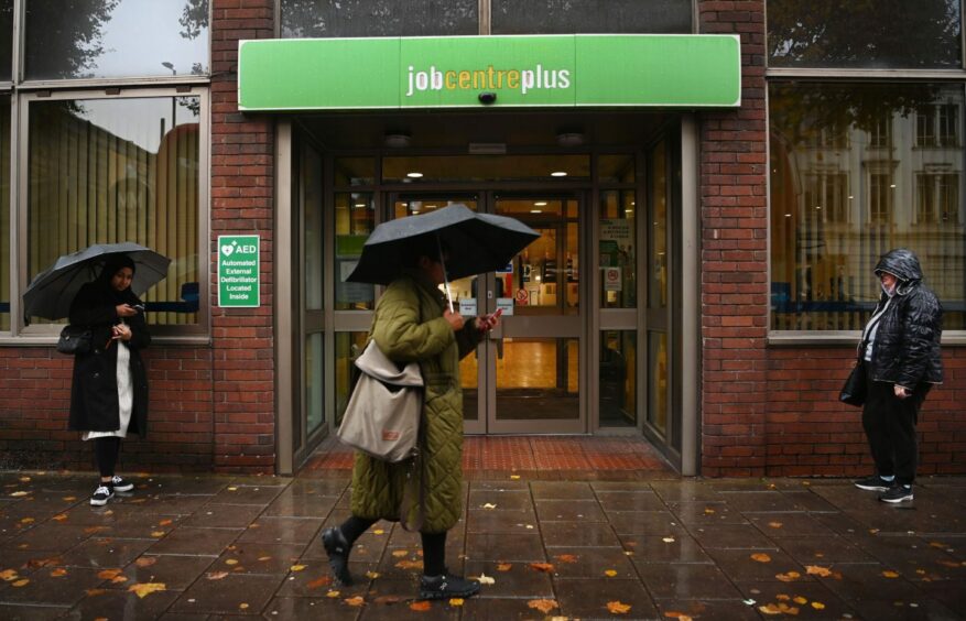 photo shows a woman with an umbrella walking past a Job Centre Plus building in the rain.