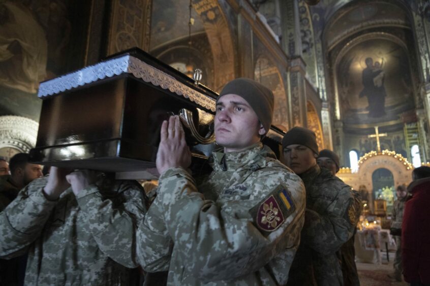 Ukrainian servicemen carrying a comrade's coffin on their shoulder.