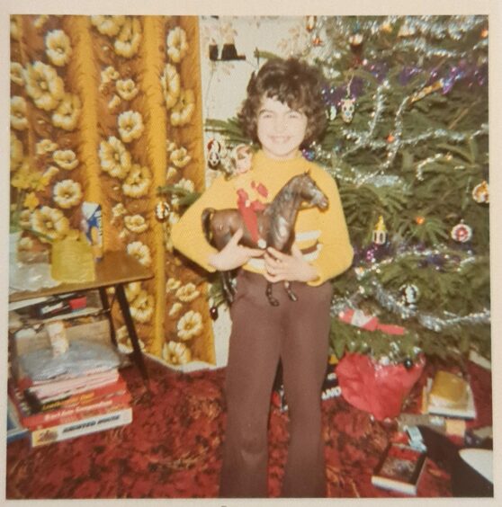 the author as a child in the 1970s with a Sindy horse, next to a Christmas tree.