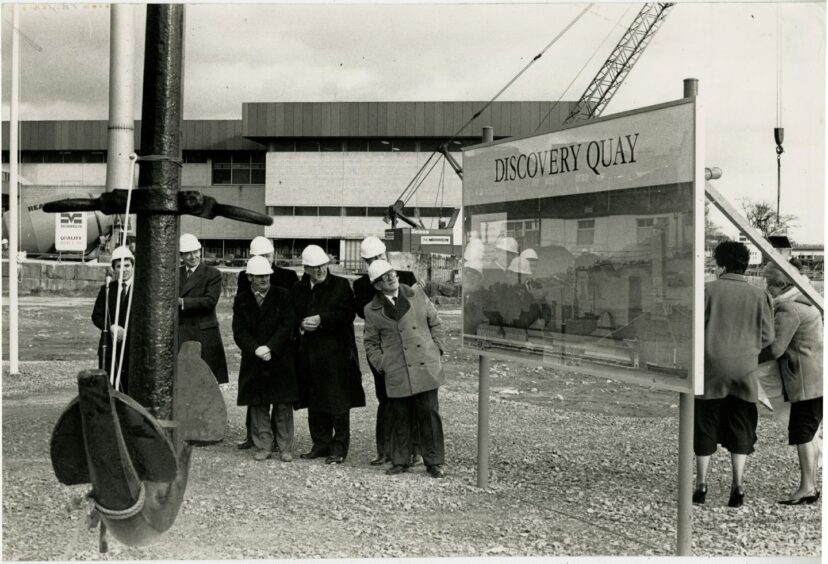 men in hard hats look at a sign saying Discovery Quay.