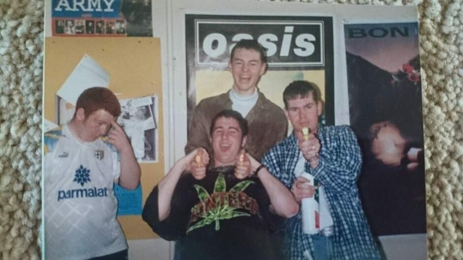 Teenage boys larking around in front of an Oasis poster.