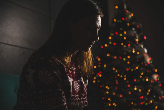 Lonely woman sitting in front of Christmas tree.