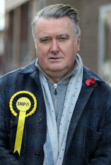 John Nicolson wearing a SNP rosette