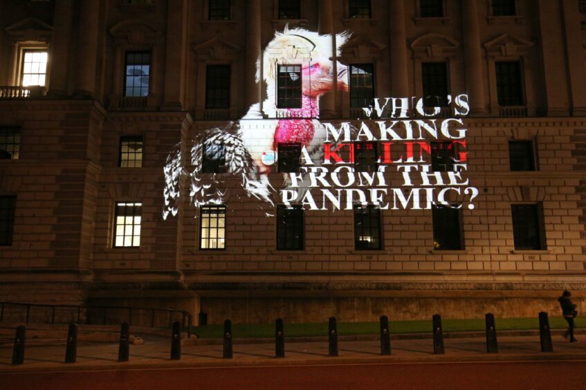 Photo shows image of Boris Johnson and the words 'Who's making a killing from the pandemic' projected onto a wall at Westminster.